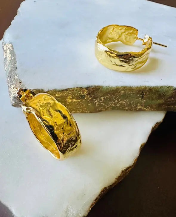 Artisanal wide textured Gold-player hoop earrings on a white stone surface