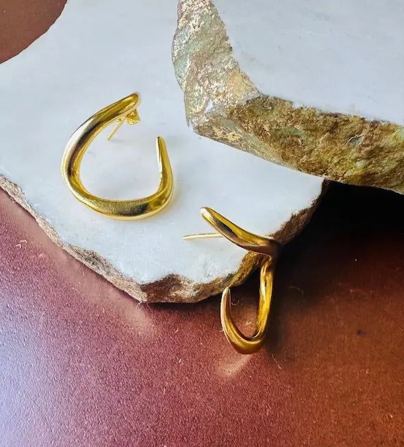Artisanal sustainable Gold-played abstract hoop earrings on a textured white stone surface