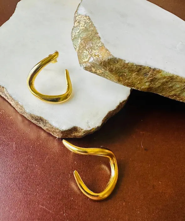 Artisanal recycled brass Gold-plated abstract hoop earrings on a textured marble surface
