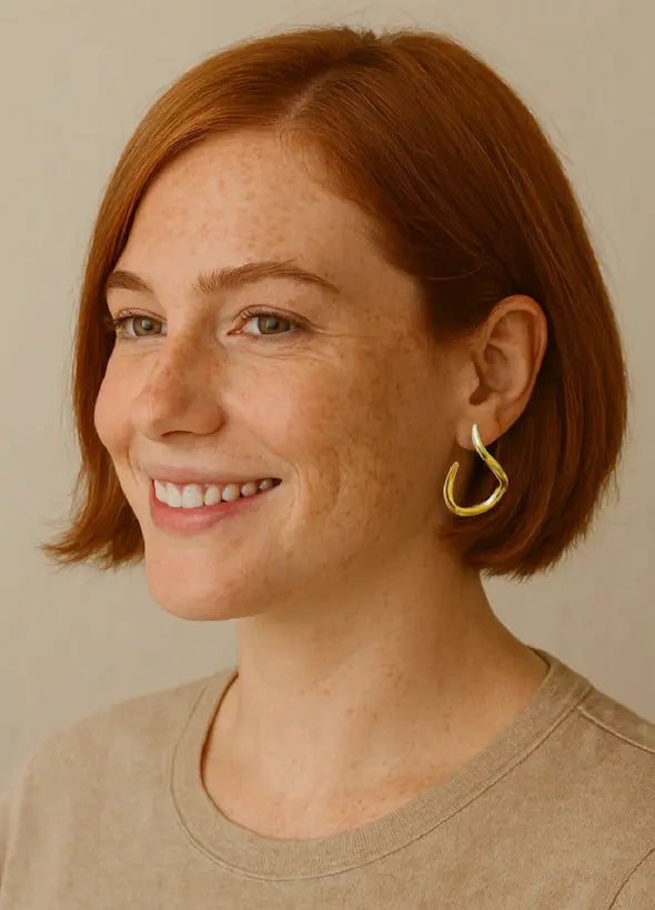 Woman with short brown hair wearing gold-plated eco-friendly handmade abstract hoop earrings against a neutral background
