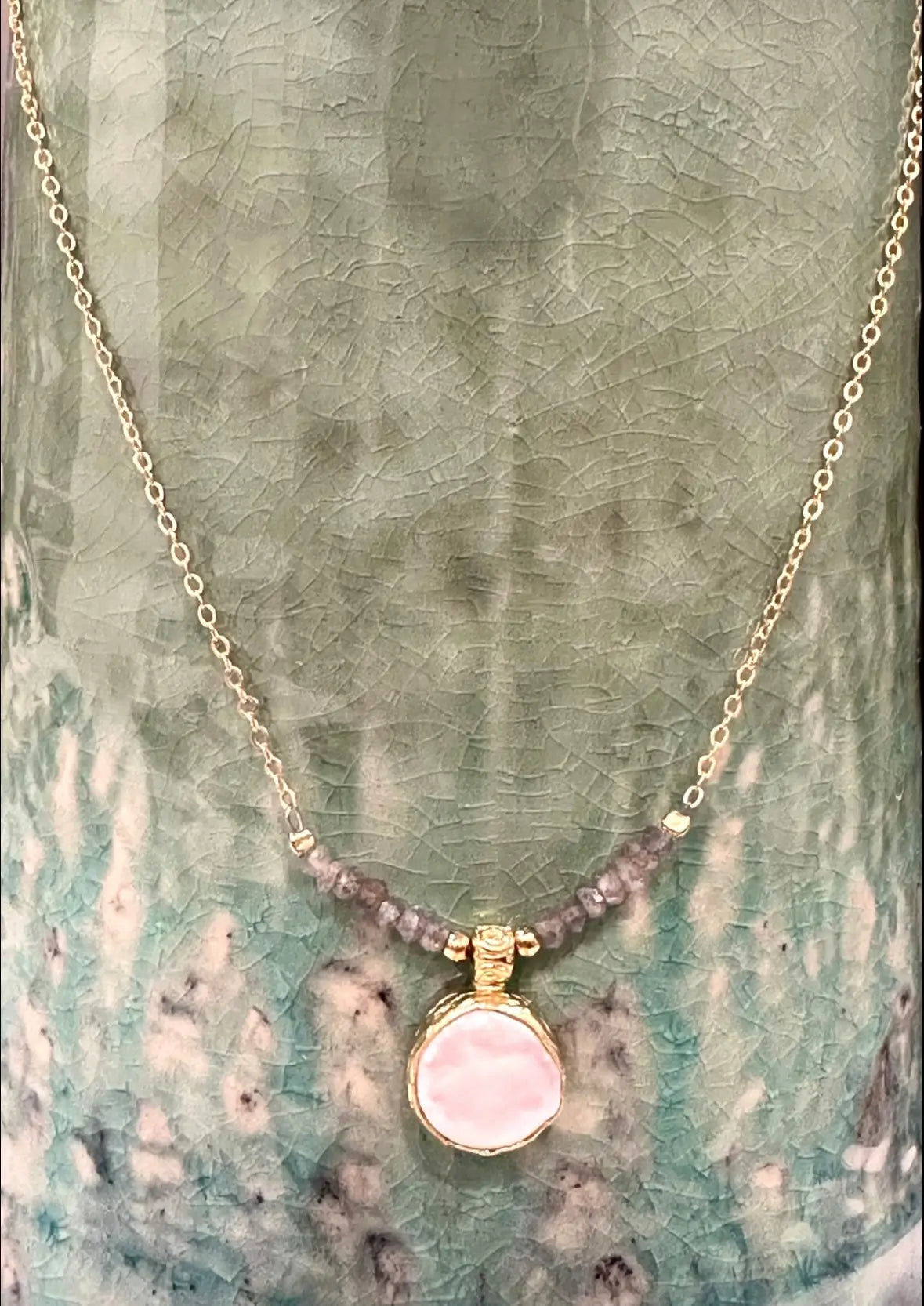 Handmade gold-plated gray beaded Necklace with a flat pearl pendant on a textured green background