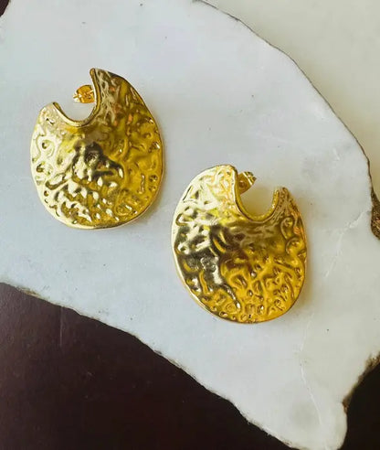 Pair of handmade contemporary eco-friendly gold-plated textured contemporary bold statement stud earrings on a white stone surface