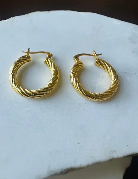 Handmade sustainable Pair of gold-plates etched hoop earrings on a white marble surface