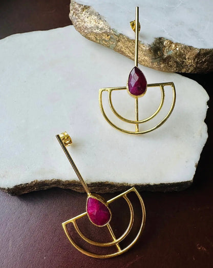 Gold-plated long geometric ruby earrings on white and brown surface