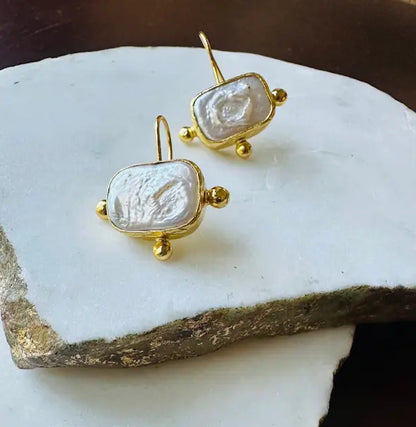 Handmade unique gold-plated flat pearl studs earrings on marble 
