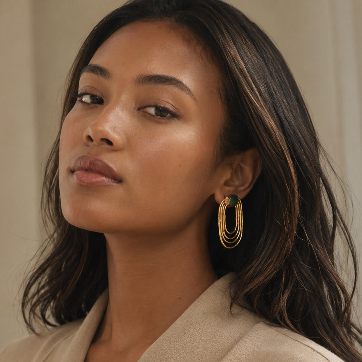 Black model wearing gold-plated sustainable ellipses emerald earrings against a neutral background