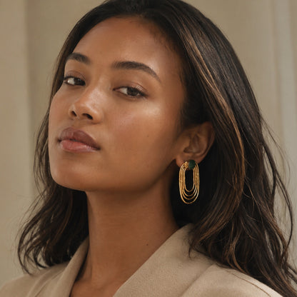Black model wearing gold-plated sustainable ellipses emerald earrings against a neutral background