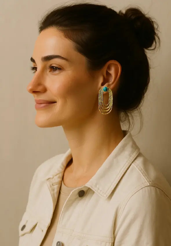 Woman wearing gold-plated sustainable ellipses emerald earrings against a neutral background