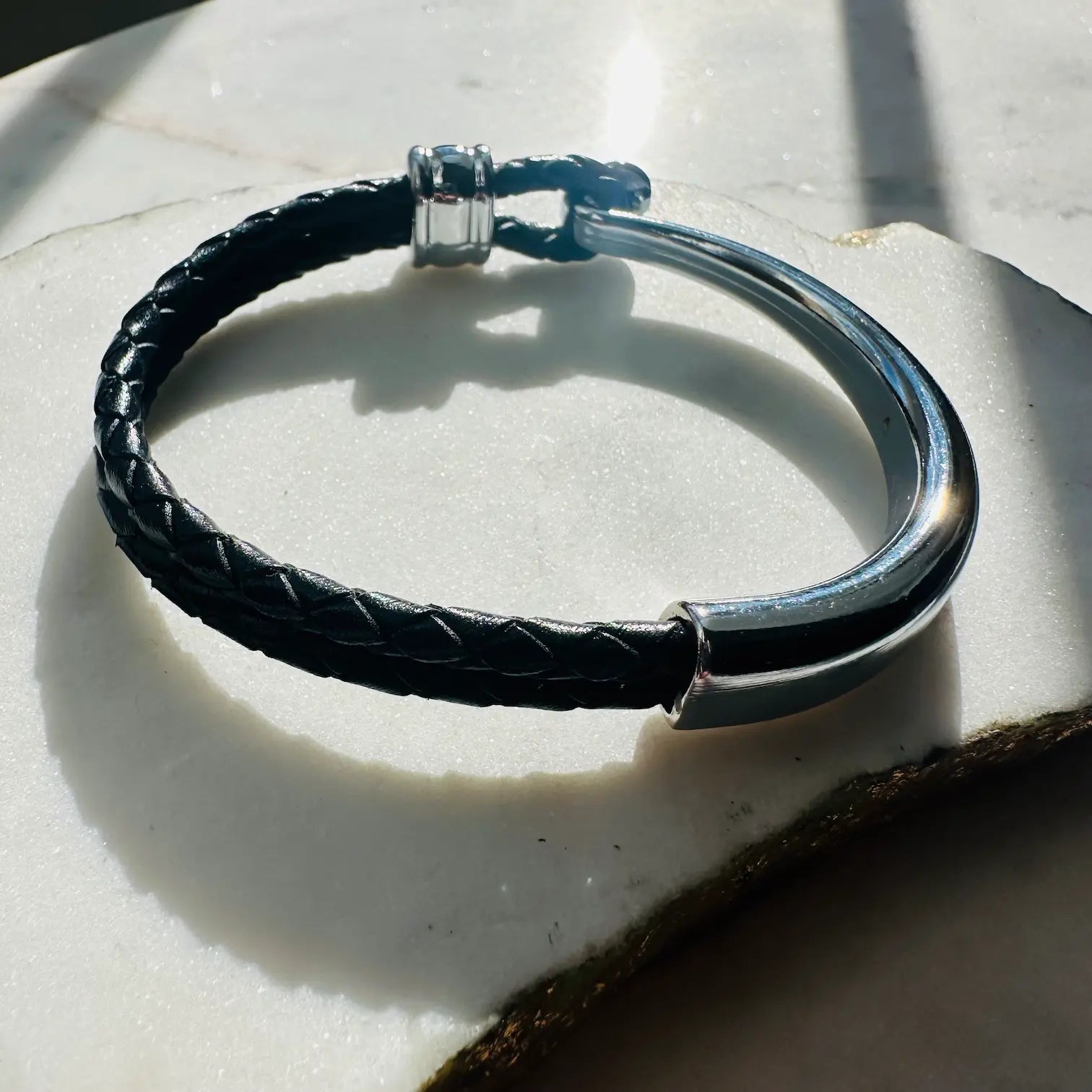 handmade men’s boho Black braided leather bracelet with silver clasp on a light stone surface