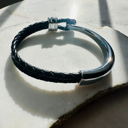 handmade men’s boho Black braided leather bracelet with silver clasp on a light stone surface