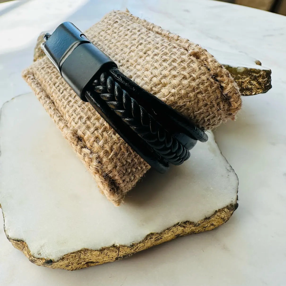 Men’s high quality handmade Black braided multi-strand leather cuff bracelet on a textured beige fabric background