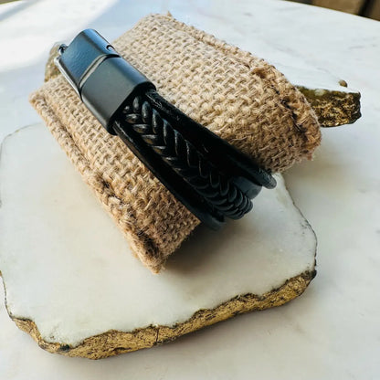 Men’s high quality handmade Black braided multi-strand leather cuff bracelet on a textured beige fabric background