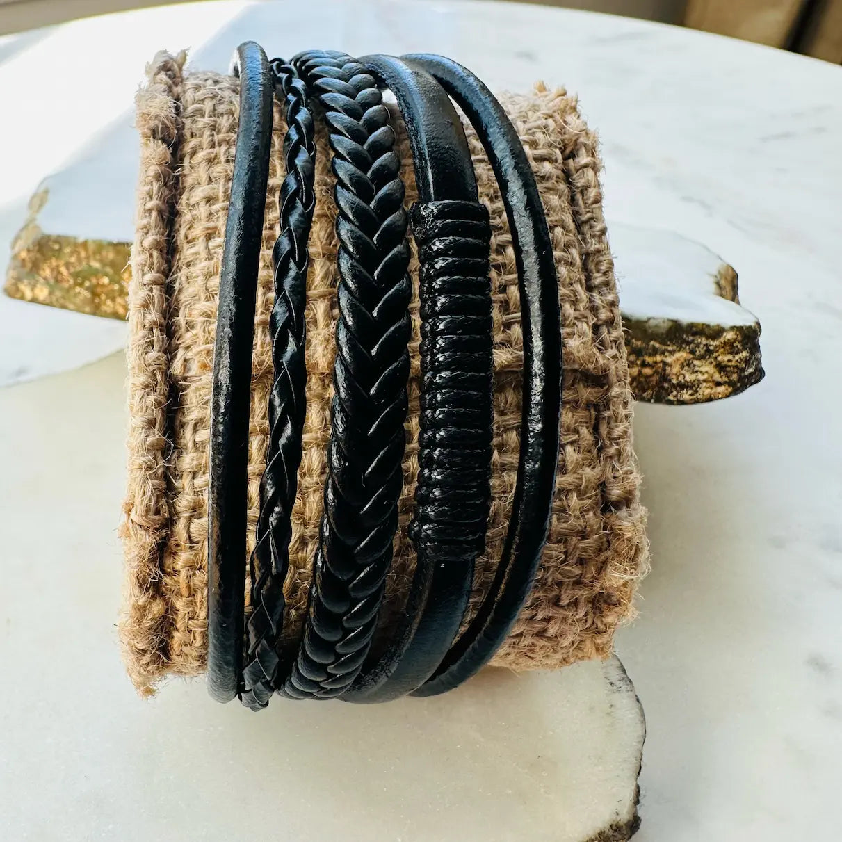 Handmade men’s rugged boho multi-strand braided black leather cuff bracelet on a textured surface