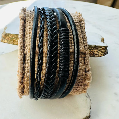 Handmade men’s rugged boho multi-strand braided black leather cuff bracelet on a textured surface