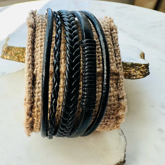Handmade men’s rugged boho multi-strand braided black leather cuff bracelet on a textured surface
