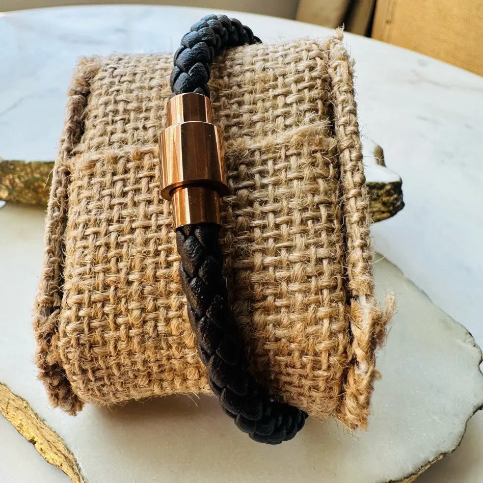 Handmade men’s brown woven bracelet with a rose gold clasp on a textured surface