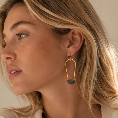 Blonde woman close up lifestyle image wearing gold plated abstract drop earrings with a faceted semi-circle labradorite center 