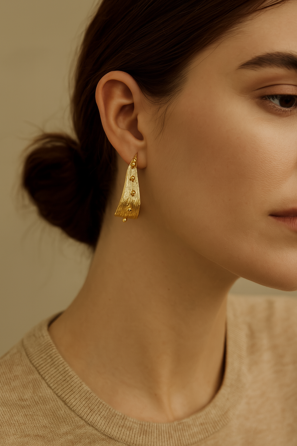 Close-up of a woman wearing gold earrings with a neutral background