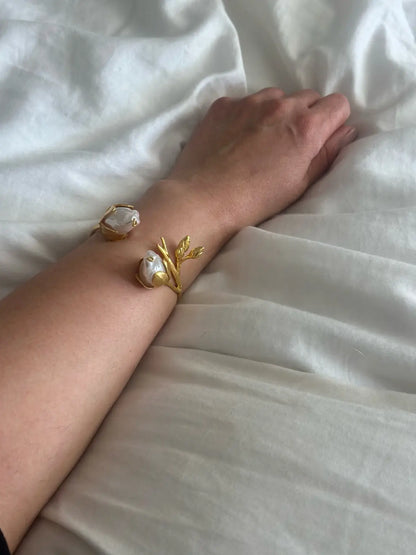 Gold bracelet with baroque pearl accents on a wrist against a white fabric background