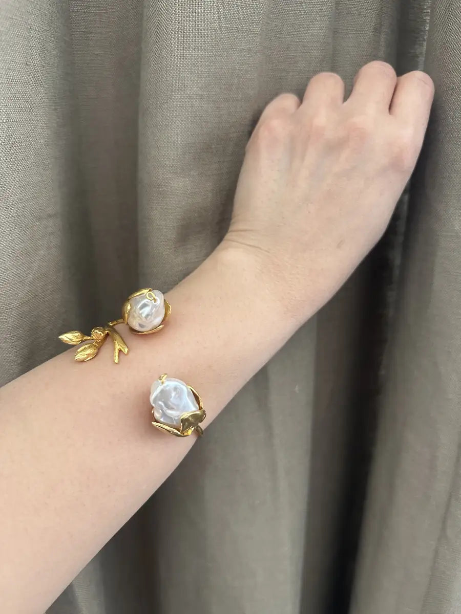 Gold cuff bracelet with baroque pearl on a floral design against a neutral background