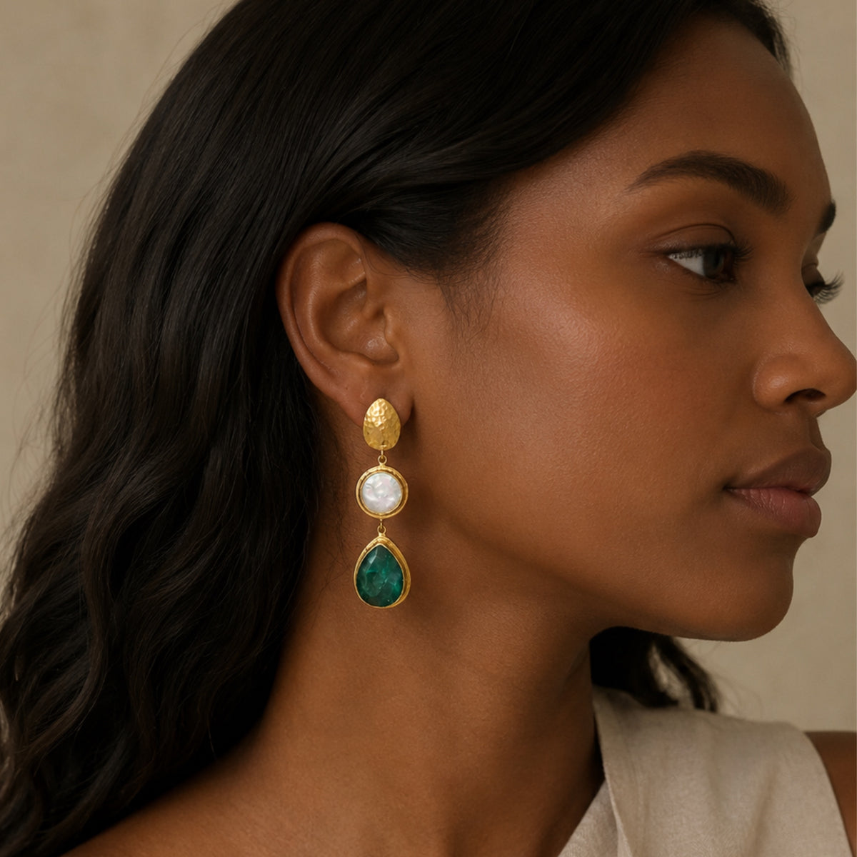 Close-up lifestyle image of African American model wearing handmade gold-plated emerald and flat pearl dangle earrings 