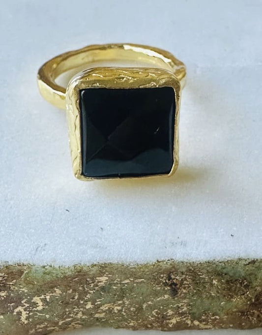 Close-up of handmade eco-friendly gold-plated square onyx ring on white marble 