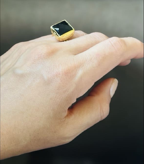 Close-up of hand wearing artisanal eco-friendly gold-plated square onyx ring against brown background 