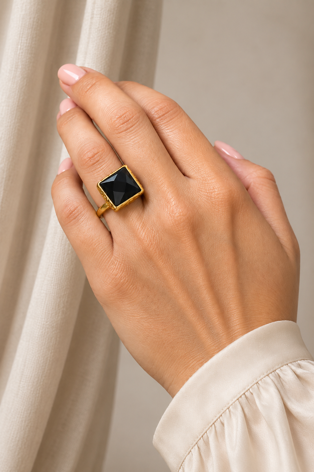 Close up of hand wearing Artisanal sustainable gold plated square onyx ring against white background