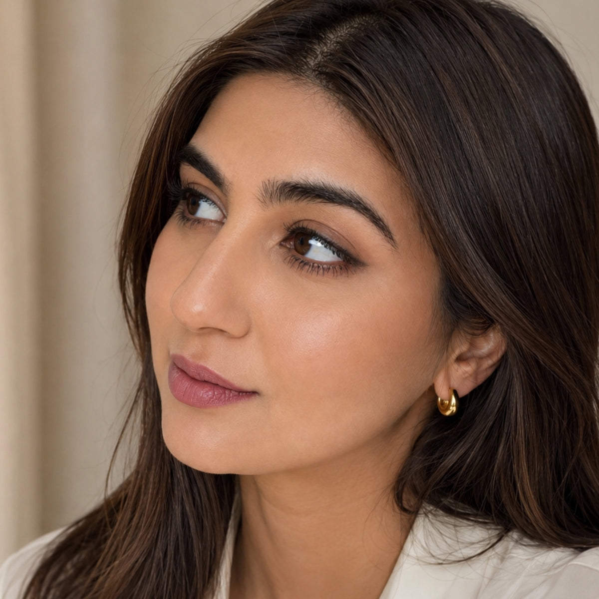 Close up of model wearing beige collared shirt and handmade gold-plated luxury hoop huggies 