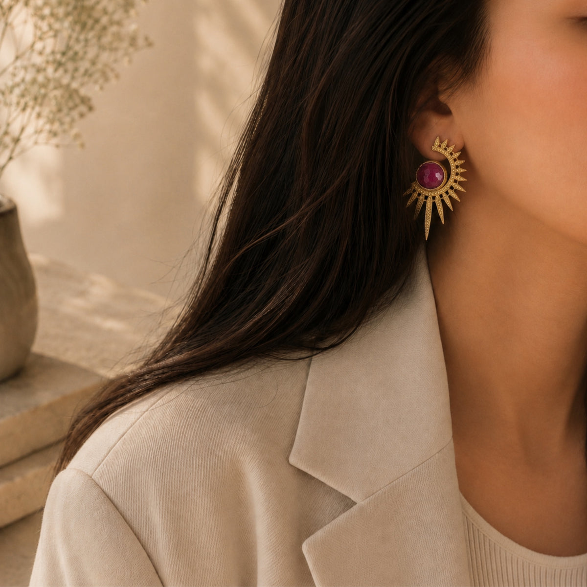 Close up of model wearing beige high end blazer and Gold plated contemporary starburst ruby statement earrings by Bebek jewels