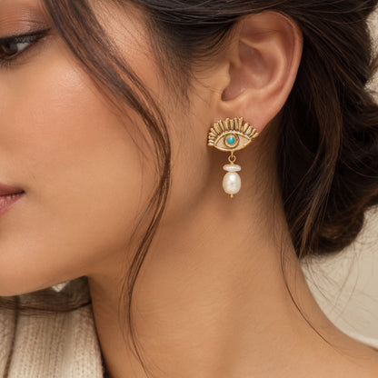 Close up of model wearing gold and turquoise evil eye earrings with pearl drops on neutral background 