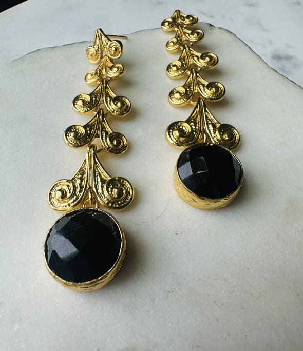 Handmade sustainable Gold-plated long earrings with black onyx stone on a marble surface zoomed in