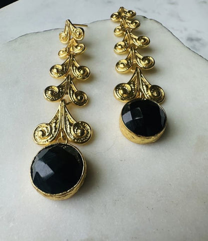 Handmade sustainable Gold-plated long earrings with black onyx stone on a marble surface zoomed in