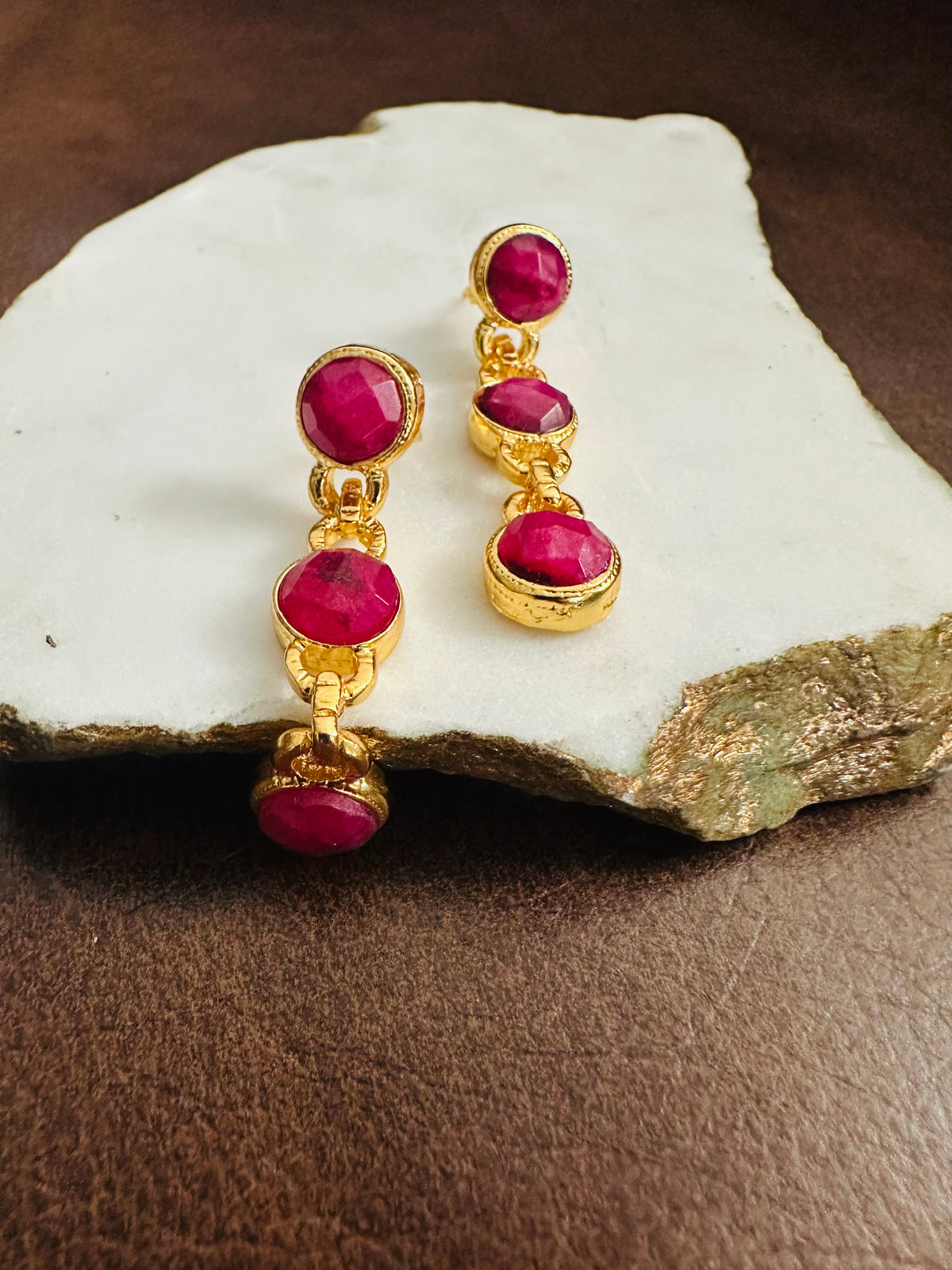 Gold dangle earrings with red ruby gemstones on a stone surface