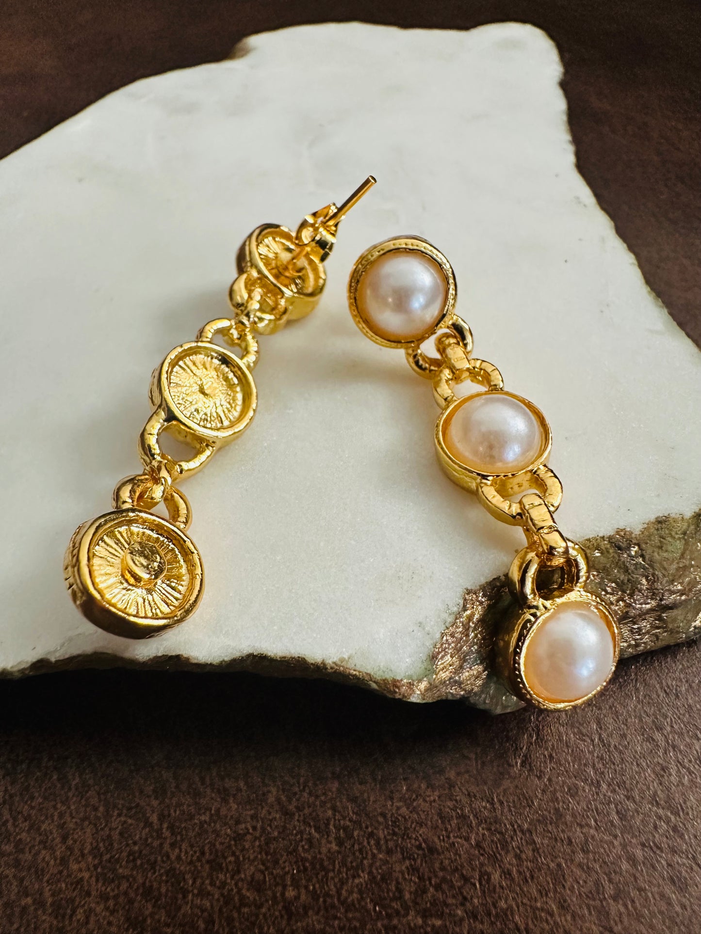 Gold earrings with pearl drops on a stone surface