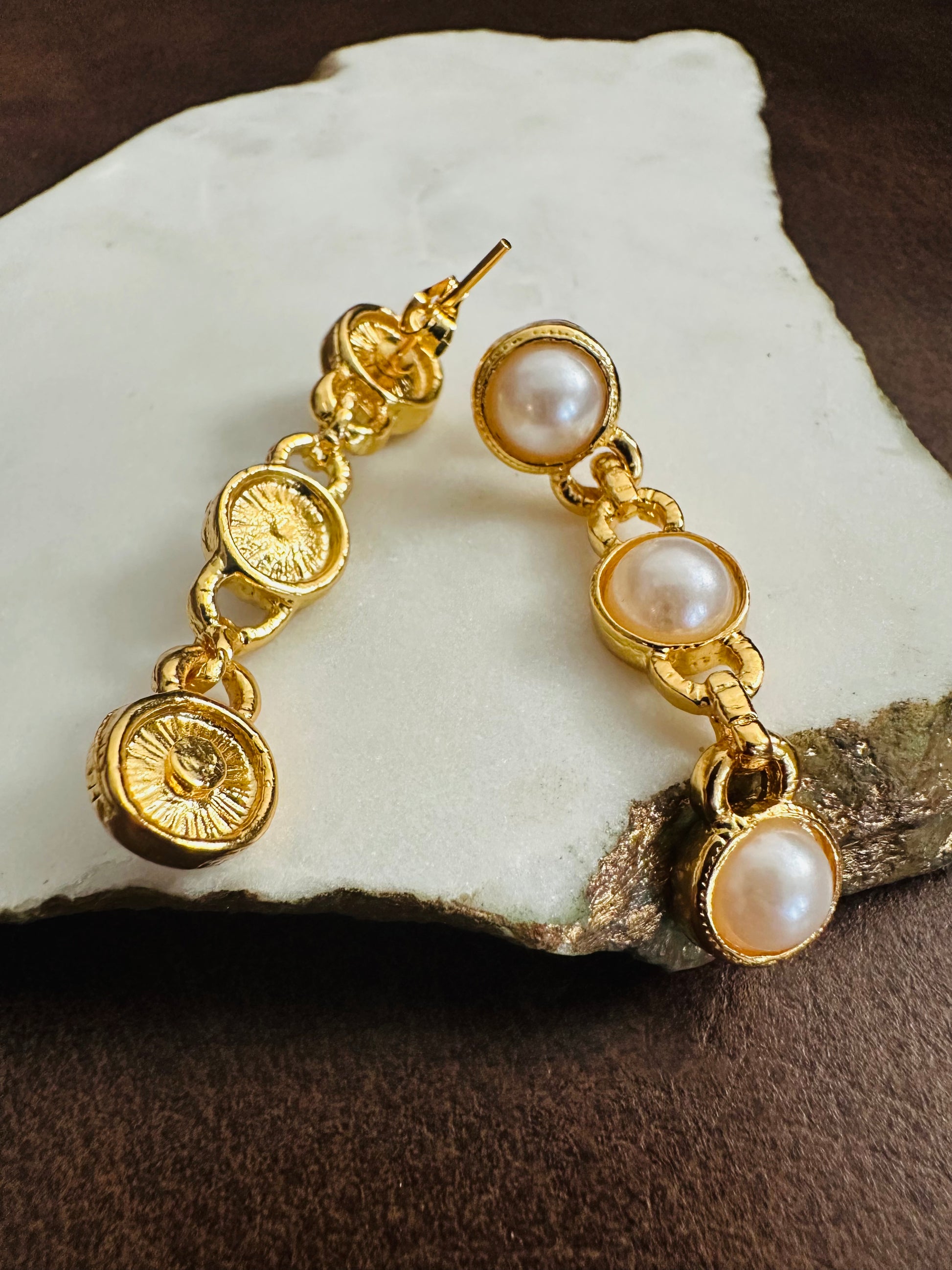 Gold earrings with pearl drops on a stone surface