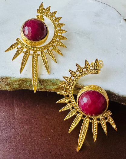Gold plated contemporary starburst ruby statement earrings by Bebek jewels On marble surface 