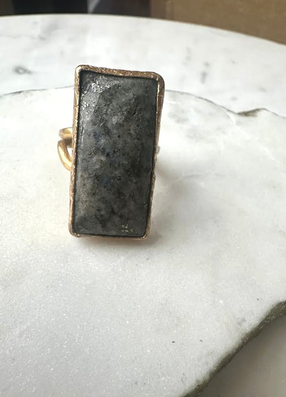 Rectangular gold-plated waterproof gray lapis lazuli cocktail ring on a marble surface