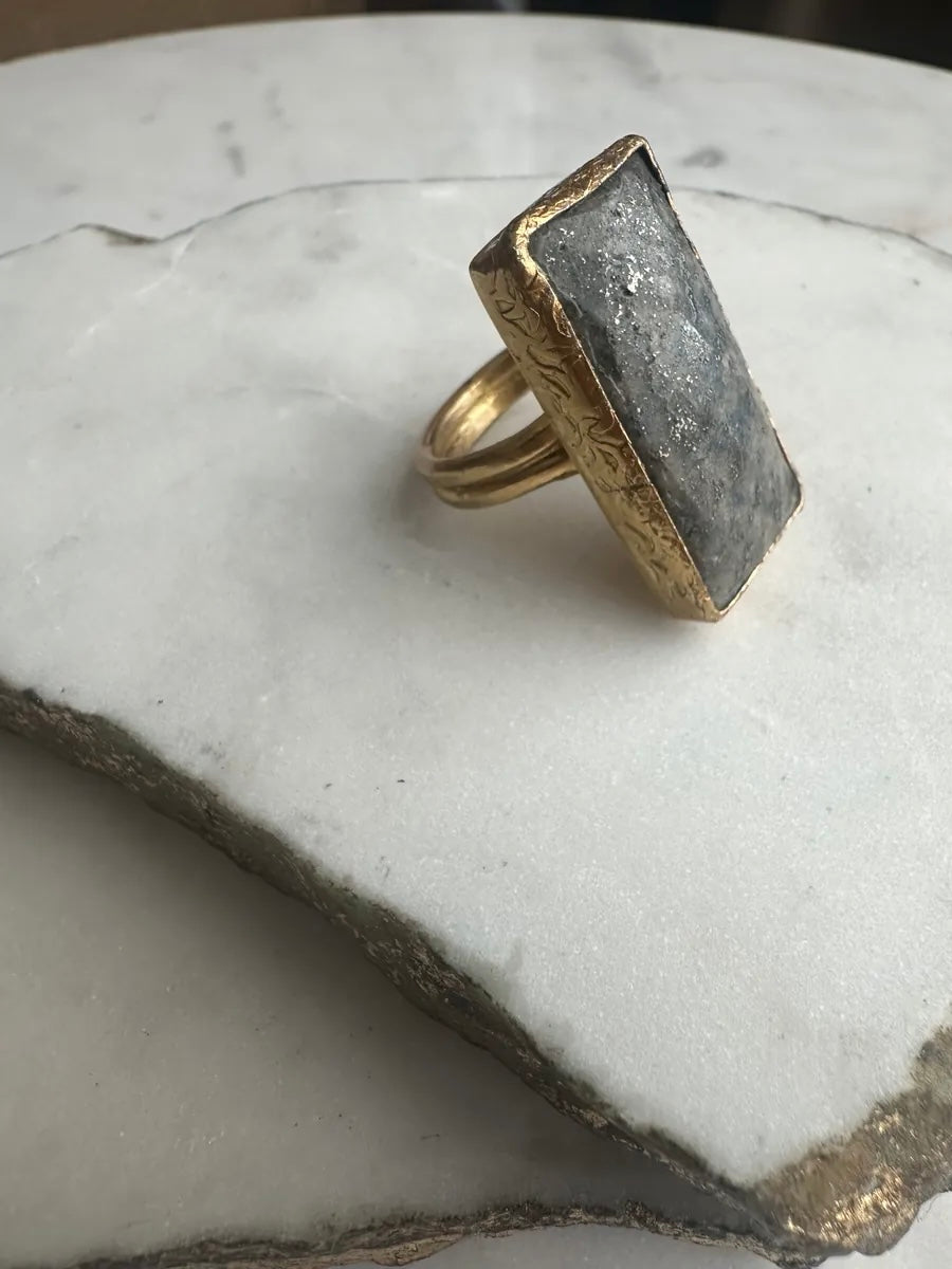 Gold-plated handmade  gray lapis lazuli cocktail ring with a rectangular stone on a marble surface