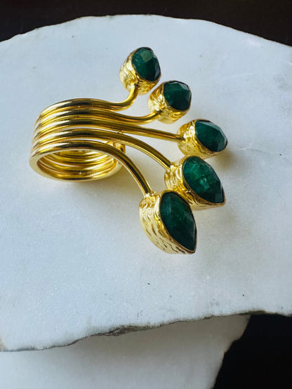 Gold-plated multi-gemstone emerald ring with green gemstones on a white stone surface