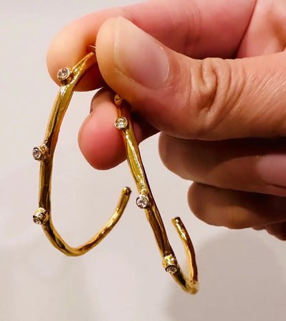 Hand holding contemporary gold-plated elongated hoop earrings with cz 