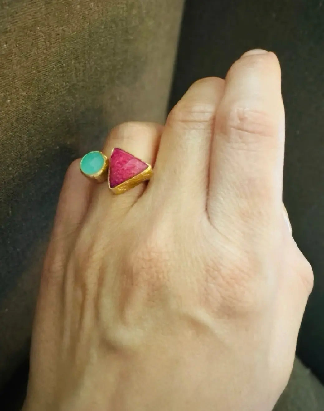 Hand wearing an artisanal sustainable gold-plated gemstone ring with a ruby triangle and aqua chalcedony round stone on a dark background