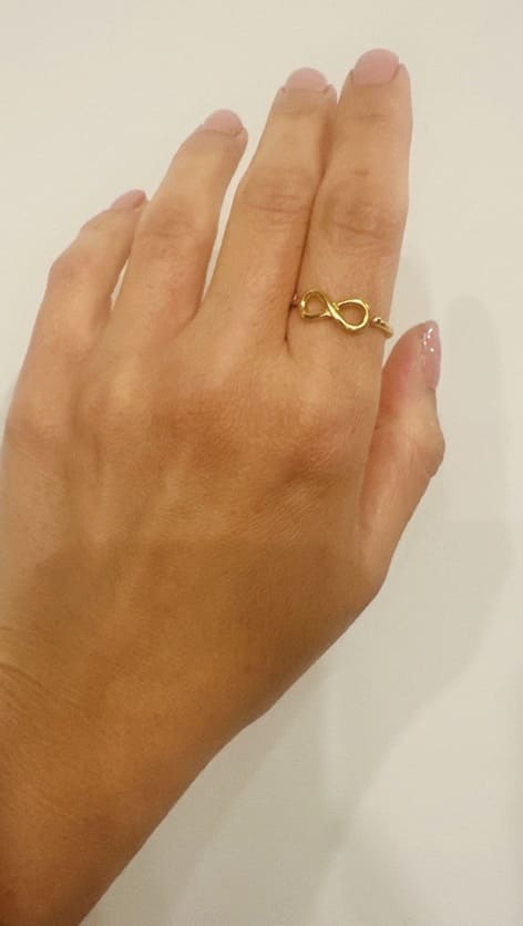 Hand wearing a gold-plated infinity ring on index finger with a plain background