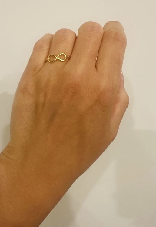 Hand wearing an infinity gold-plated waterproof infinity ring on ring finger against a plain background