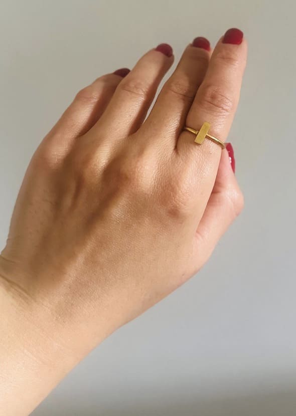 Hand wearing an artisanal gold-plated waterproof minimal ring on a plain background