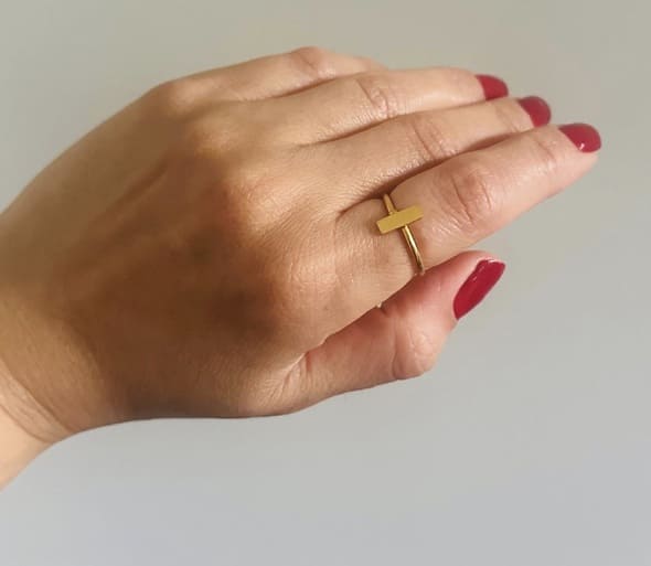 Hand wearing a Handmade gold-plated waterproof bar ring with red nail polish on a neutral background