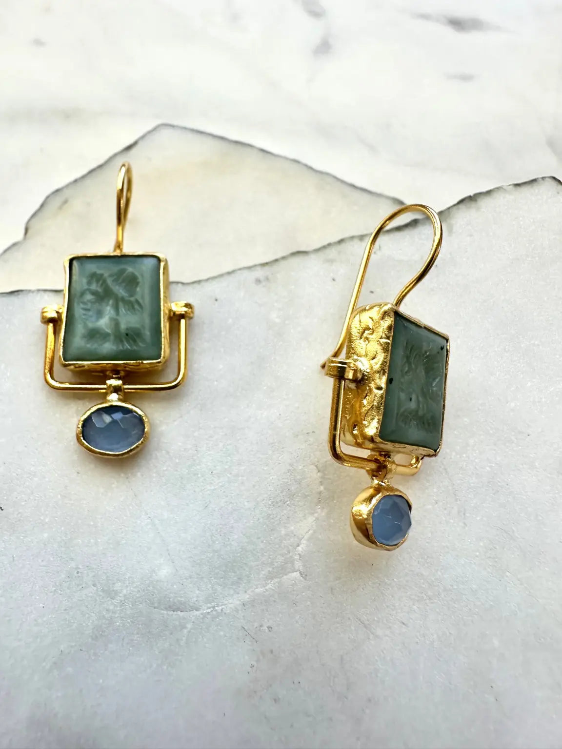 Goldplated contemporary earrings with jade green and blue chalcedony stones on a marble surface