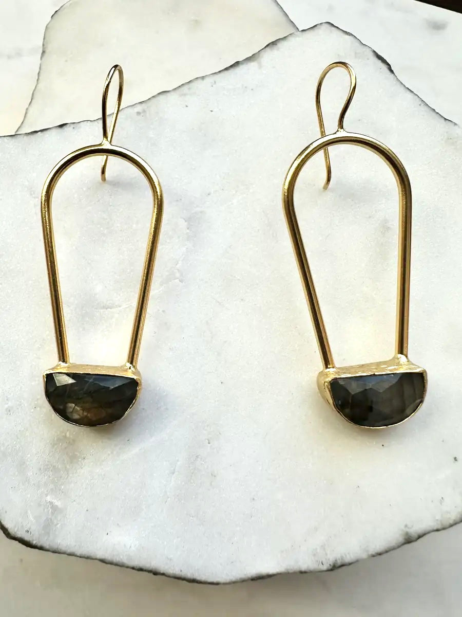 Gold-plated earrings with gray labradorite stones on a white stone surface