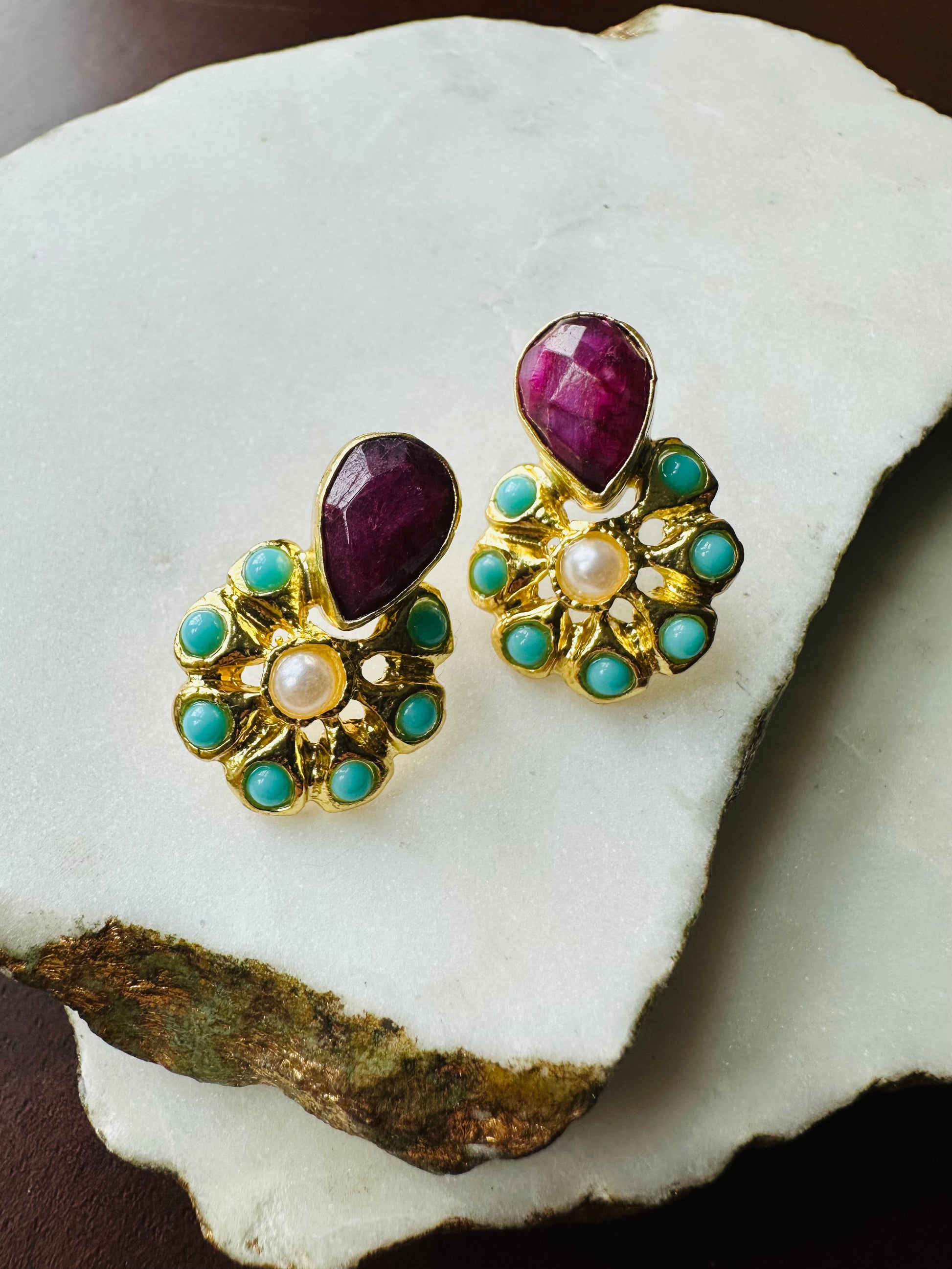 Pair of gold-plated stud earrings with ruby, turquoise, and pearl gemstones on a white background.