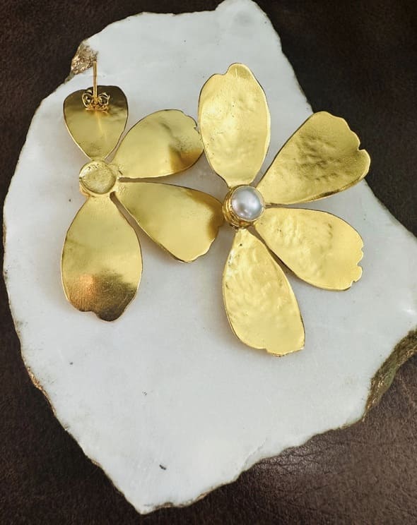Handmade sustainable Gold-plated flower-shaped earring with pearl on a white stone background with be faced down 